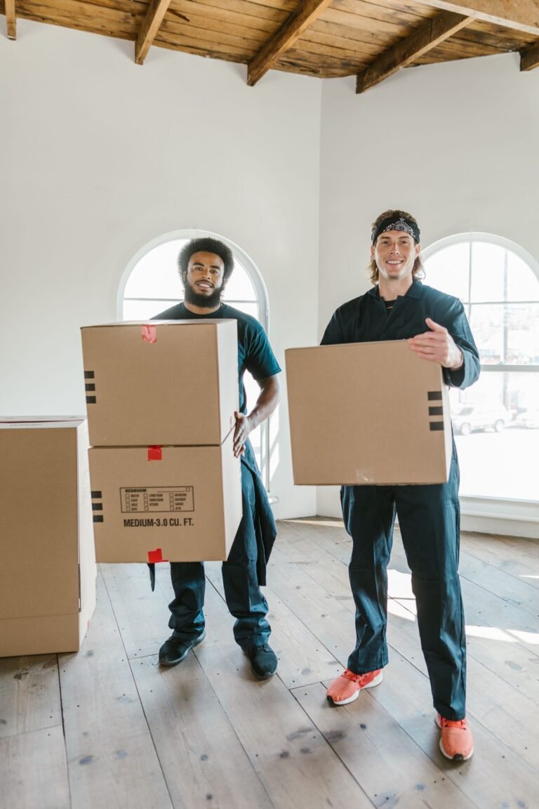 Two packers and movers carrying labelled cardboard boxes into a newly built house – shifting checklist by GharVistar